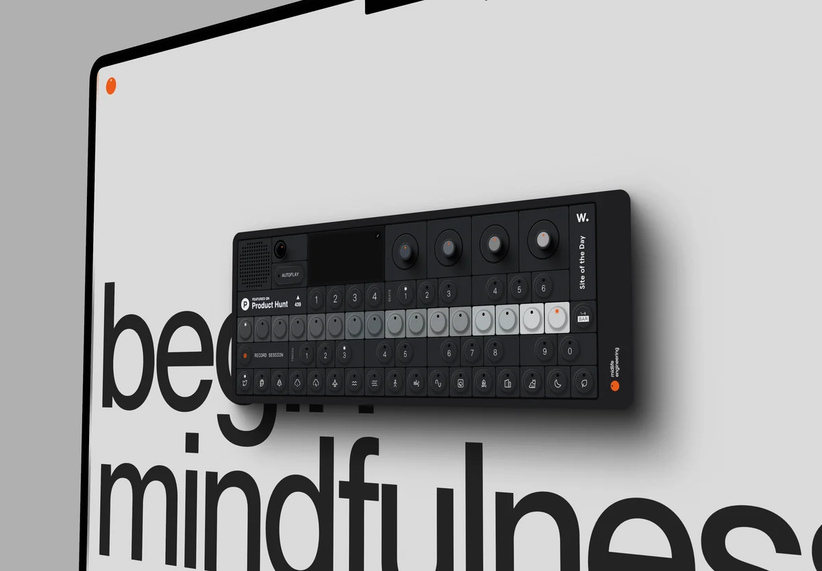 A close view of a laptop screen on pale grey, a black synthesizer on the page above the words begin mindfulness.