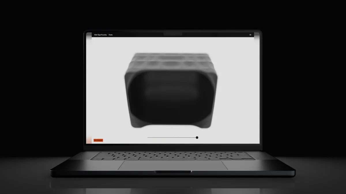 A black laptop open on a dark floor, a soft grey object on its screen.